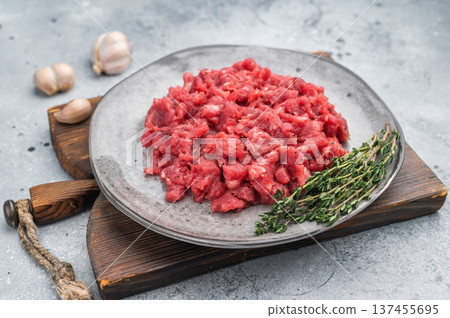 Raw chopped beef veal meat served with herbs on rustic plate against textured concrete backdrop perfect for culinary ads and protein food visuals. Raw chopped beef veal meat served with herbs on rustic plate against textured concrete backdrop perfect for culinary ads and protein food visuals. 137455695