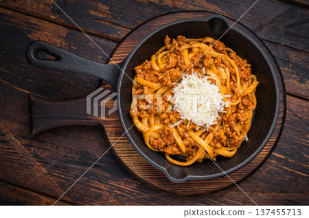 Classic pasta bolognese with savory meat ragu and parmesan shreds served in rustic skillet on vintage wooden surface with herbs. 137455713