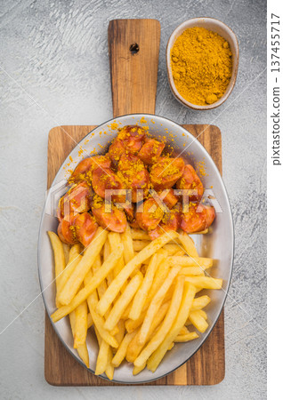 Traditional currywurst topped with curry spice and pommes on concrete surface great for German street food themes and high quality photography. Traditional currywurst topped with curry spice and pommes on concrete surface great for German street food themes and high quality photography. 137455717