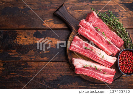 Raw beef short ribs with thyme and pink peppercorns on a dark wooden cutting board. Excellent for a BBQ recipe or restaurant menu. Raw beef short ribs with thyme and pink peppercorns on a dark wooden cutting board. Excellent for a BBQ recipe or restaurant menu. 137455720