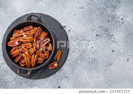 Closeup of pecans in a cast iron pan placed on a wooden board over a grey artistic surface giving a rustic gourmet feel ideal for culinary stock imagery Closeup of pecans in a cast iron pan placed on a wooden board over a grey artistic surface giving a rustic gourmet feel ideal for culinary stock imagery 137455727