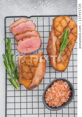 Tender grilled duck breast and sliced meat on cooling rack with herbs and pink salt over bright grey texture ideal for culinary visuals. Tender grilled duck breast and sliced meat on cooling rack with herbs and pink salt over bright grey texture ideal for culinary visuals. 137455729