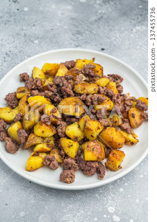 Crispy fried potatoes with ground beef served on a white plate, hearty homemade hash on a rustic grey background.. Crispy fried potatoes with ground beef served on a white plate, hearty homemade hash on a rustic grey background.. 137455736