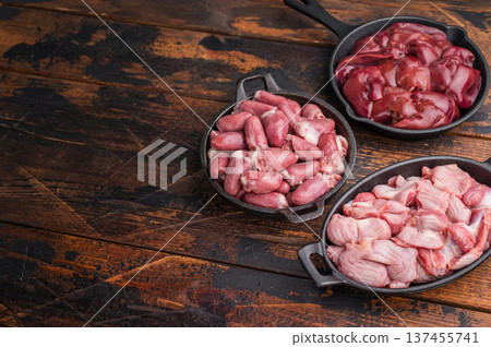 Fresh raw poultry offal assortment with duck hearts, liver, and gizzards on dark rustic wood table, organic cooking concept. Fresh raw poultry offal assortment with duck hearts, liver, and gizzards on dark rustic wood table, organic cooking concept. 137455741