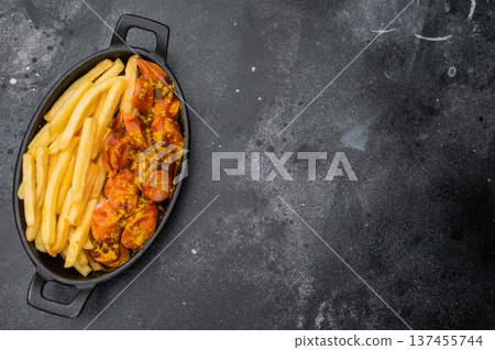 German currywurst with fries in a cast iron pan on dark background perfect for street food visuals fast food ads and stock images. German currywurst with fries in a cast iron pan on dark background perfect for street food visuals fast food ads and stock images. 137455744