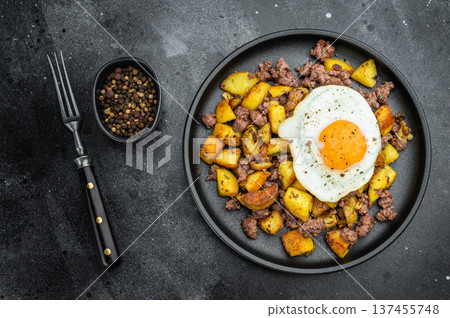Savory skillet style hash of diced potatoes, ground beef and sunny egg on dark textured backdrop with fork for cooking and meal prep photos. Savory skillet style hash of diced potatoes, ground beef and sunny egg on dark textured backdrop with fork for cooking and meal prep photos. 137455748