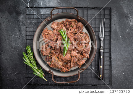 Rustic braised moose venison stew, shredded and savory, plated with fresh rosemary on a metal dish over dark stone background 137455750
