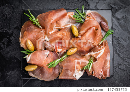 Appetizer of Sliced Ham and Olives garnished with rosemary, set on a dark rustic surface. Traditional Mediterranean snack. 137455753