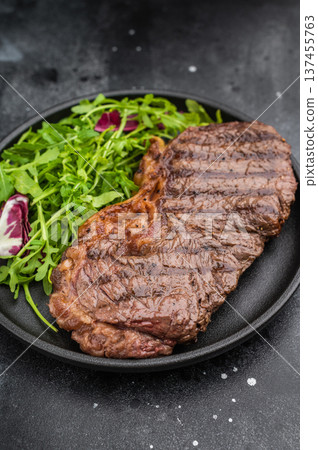 Roasted dry aged New York strip steak served with fresh arugula on textured dark stone, highlighting rich flavor and perfect grill marks. Roasted dry aged New York strip steak served with fresh arugula on textured dark stone, highlighting rich flavor and perfect grill marks. 137455763