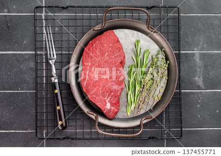 Uncooked beef knuckle sirloin tip steak with rosemary, thyme and garlic in skillet. Fresh red meat ingredient prepared for cooking on dark background. 137455771