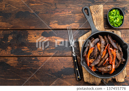 Beef stir fry with bell peppers cooked in cast iron skillet on rustic wooden table. Chinese pepper steak style dish with copy space. Beef stir fry with bell peppers cooked in cast iron skillet on rustic wooden table. Chinese pepper steak style dish with copy space. 137455776