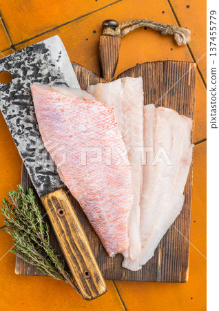 Raw rosefish or snapper fillets with herbs and cleaver on wooden board. Seafood preparation scene with bright background. Raw rosefish or snapper fillets with herbs and cleaver on wooden board. Seafood preparation scene with bright background. 137455779