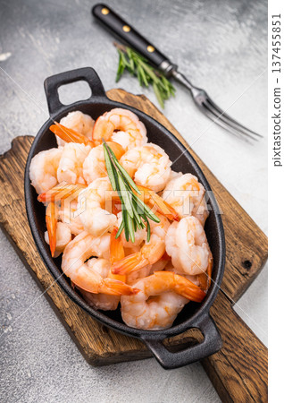 A plate of shrimp is on a wooden cutting board with a fork and a sprig of rosemary A plate of shrimp is on a wooden cutting board with a fork and a sprig of rosemary 137455851