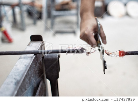 Glassblowing in a glass workshop, cutting hot glass with scissors 137457959
