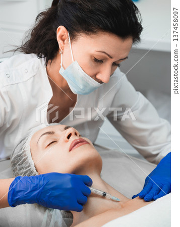 Woman beautician injecting rejuvenating filler into the neck of a female patient in a beauty clinic, close-up Woman beautician injecting rejuvenating filler into the neck of a female patient in a beauty clinic, close-up 137458097