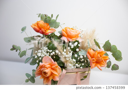 Elegant bouquet of orange roses with eucalyptus leaves placed in a decorative gift box on a white background. Celebration, appreciation, romance, floristry craft, and thoughtful present for special Elegant bouquet of orange roses with eucalyptus leaves placed in a decorative gift box on a white background. Celebration, appreciation, romance, floristry craft, and thoughtful present for special 137458399