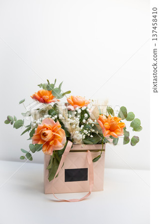 Orange roses arranged in a decorative gift box with eucalyptus and delicate filler flowers on a minimal white background. Celebration, appreciation, romance, floral design, and elegant gift giving Orange roses arranged in a decorative gift box with eucalyptus and delicate filler flowers on a minimal white background. Celebration, appreciation, romance, floral design, and elegant gift giving 137458410