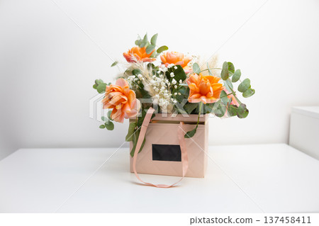 Orange roses arranged in a decorative gift box with eucalyptus and delicate filler flowers on a minimal white background. Celebration, appreciation, romance, floral design, and elegant gift giving Orange roses arranged in a decorative gift box with eucalyptus and delicate filler flowers on a minimal white background. Celebration, appreciation, romance, floral design, and elegant gift giving 137458411