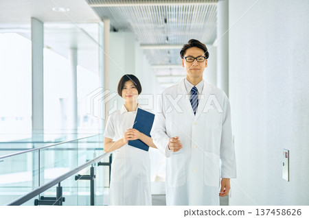 A smiling Japanese male doctor and female nurse walking down a hospital corridor. An image of teamwork and trust. 137458626