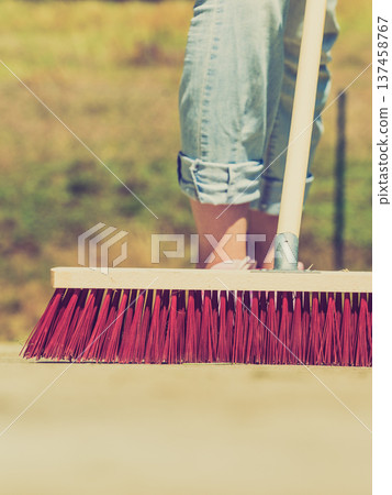 Woman using broom to clean up backyard patio Woman using broom to clean up backyard patio 137458767