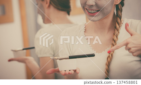 Happy young woman applying mud mask on face Happy young woman applying mud mask on face 137458801