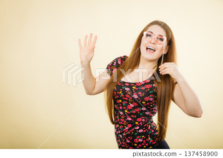 Happy woman holding fake eyeglasses on stick Happy woman holding fake eyeglasses on stick 137458900