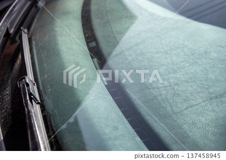Windshield shows dirt and water spots after rain in the morning light outside a parking area. Visible wiper streaks and reflections Windshield shows dirt and water spots after rain in the morning light outside a parking area. Visible wiper streaks and reflections 137458945