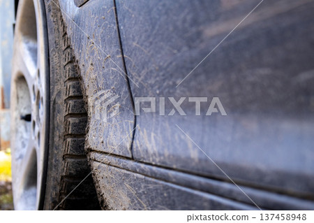 A close view shows dirt and mud on the side of a car, highlighting the wear from driving on roads. The background is blurred and not clear 137458948