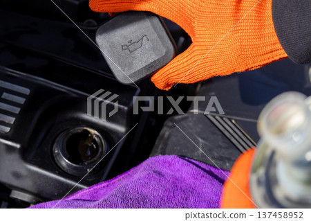 A mechanic holds an engine cover above the engine bay. He works on a vehicle in a garage during daylight hours A mechanic holds an engine cover above the engine bay. He works on a vehicle in a garage during daylight hours 137458952