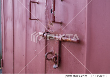 A metal gate is closed with a latch and lock in a residential area. It shows wear and tear from years of use 137458962