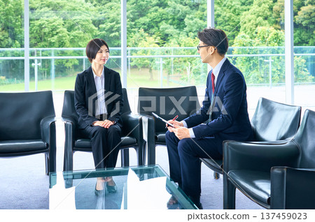 A woman in a recruitment suit and her interviewer are having a job interview in a bright office lobby. A woman in a recruitment suit and her interviewer are having a job interview in a bright office lobby. 137459023