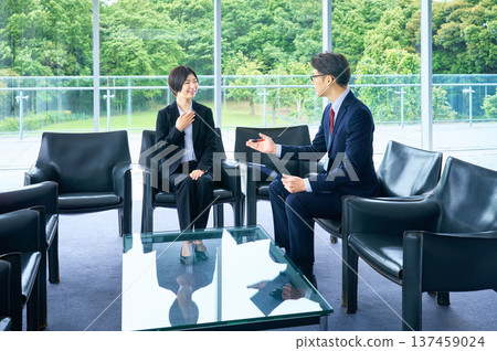 一位身穿職業裝的女士和她的面試官正在明亮的辦公大廳裡進行面試。 137459024