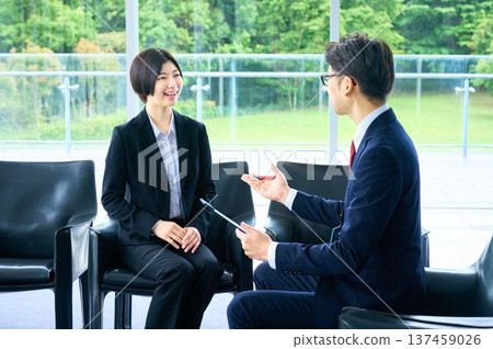 一位身穿職業裝的女士和她的面試官正在明亮的辦公大廳裡進行面試。 137459026