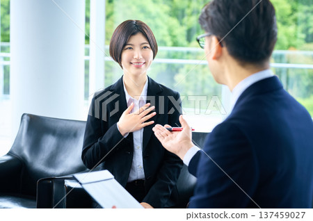 一位身著職業裝的女士在求職面試中自信地推銷自己，一位男面試官認真地聽著。 137459027