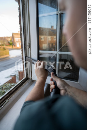 Spring home cleaning. Man vacuums plastic window frame. 137459082