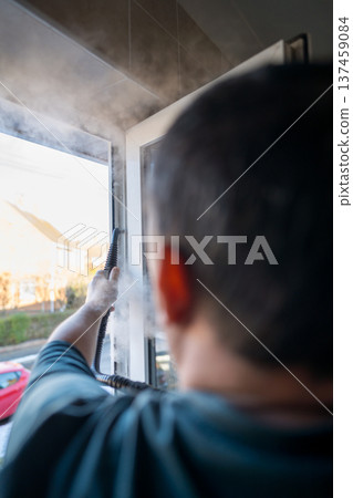Cleaning the window. A man with steam device removes dirt from the plastic window frame. 137459084