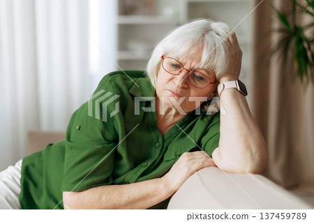 Senior woman sitting on sofa holding head with thoughtful expression at home Senior woman sitting on sofa holding head with thoughtful expression at home 137459789