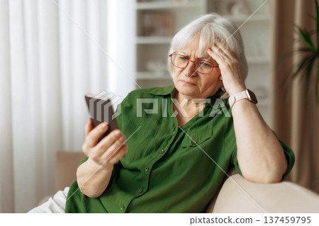 Senior woman with glasses looking at smartphone with worried expression at home 137459795