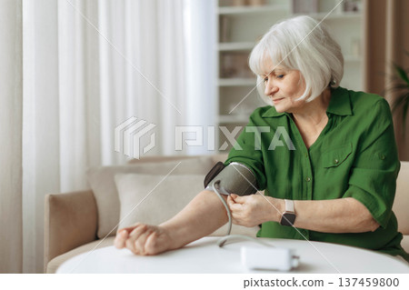 Senior woman adjusting blood pressure cuff on arm while sitting at home Senior woman adjusting blood pressure cuff on arm while sitting at home 137459800