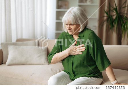 Senior woman touching chest while sitting on sofa at home 137459853