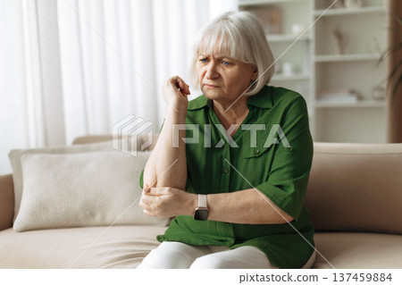Senior woman touching painful elbow while sitting on sofa at home 137459884