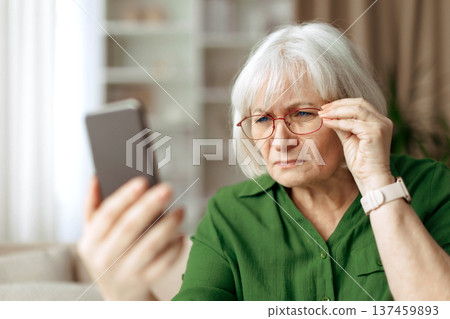 Senior woman adjusting eyeglasses while looking at smartphone screen Senior woman adjusting eyeglasses while looking at smartphone screen 137459893