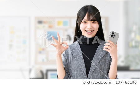 A young woman/businesswoman holding a smartphone and making an OK pose 137460196