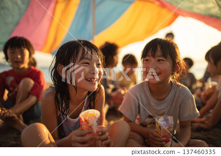 夕陽西下，孩子們在沙灘上休息喝果汁，臉上洋溢著笑容。 137460335