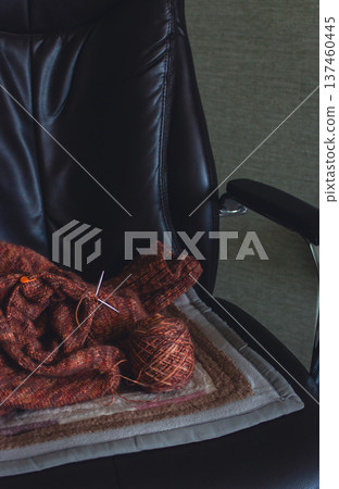 Unfinished melange brown sweater with knitting needles on armchair. Knitting needles and balls of warm melange yarn. Knitting work in process. Knitting hobby. Knitwear concept. Knitted fashion. Unfinished melange brown sweater with knitting needles on armchair. Knitting needles and balls of warm melange yarn. Knitting work in process. Knitting hobby. Knitwear concept. Knitted fashion. 137460445