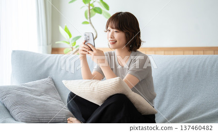 A woman sitting on a sofa in the living room and using a smartphone A woman sitting on a sofa in the living room and using a smartphone 137460482