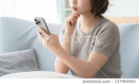 一位女士坐在客廳的沙發上,正在使用智慧型手機 一位女士坐在客廳的沙發上,正在使用智慧型手機 137460483