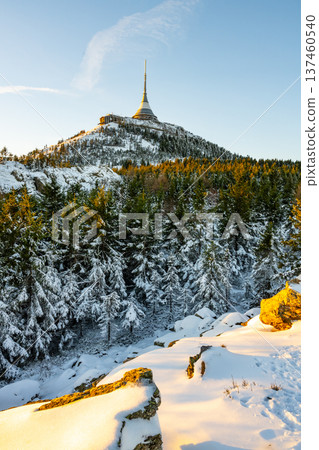 Snow covers the ground and trees near a mountain with a hotel on top. The sky shows light as the sun rises. The scene captures winter's chill and the beauty of nature. Snow covers the ground and trees near a mountain with a hotel on top. The sky shows light as the sun rises. The scene captures winter's chill and the beauty of nature. 137460540