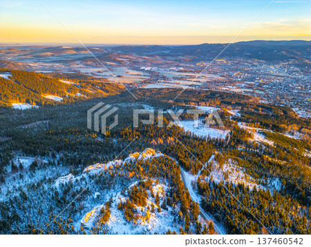 Aerial view shows a winter morning landscape in Liberec. Snow covers trees and fields. The sunlight creates shadows across the mountains and town below. Aerial view shows a winter morning landscape in Liberec. Snow covers trees and fields. The sunlight creates shadows across the mountains and town below. 137460542