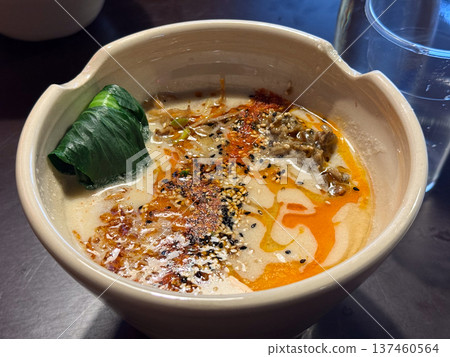 Creamy ramen soup with sesame, chili oil and greens served in ceramic bowl. Asian comfort food, japanese noodle cuisine and warm restaurant dining atmosphere. 137460564